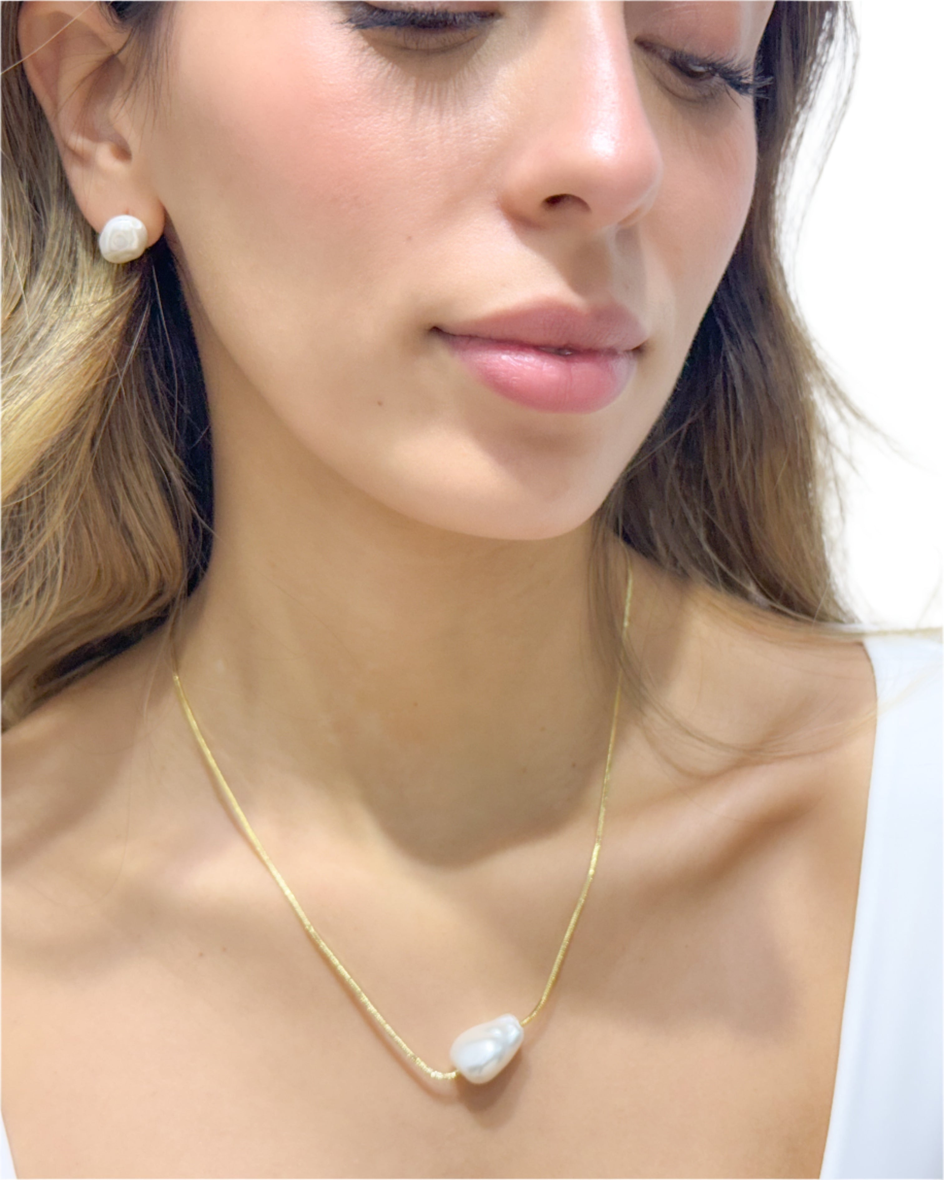 Woman wearing a gold necklace and earrings against a plain background